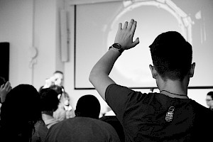 A hand raised in the crowd at a public talk.