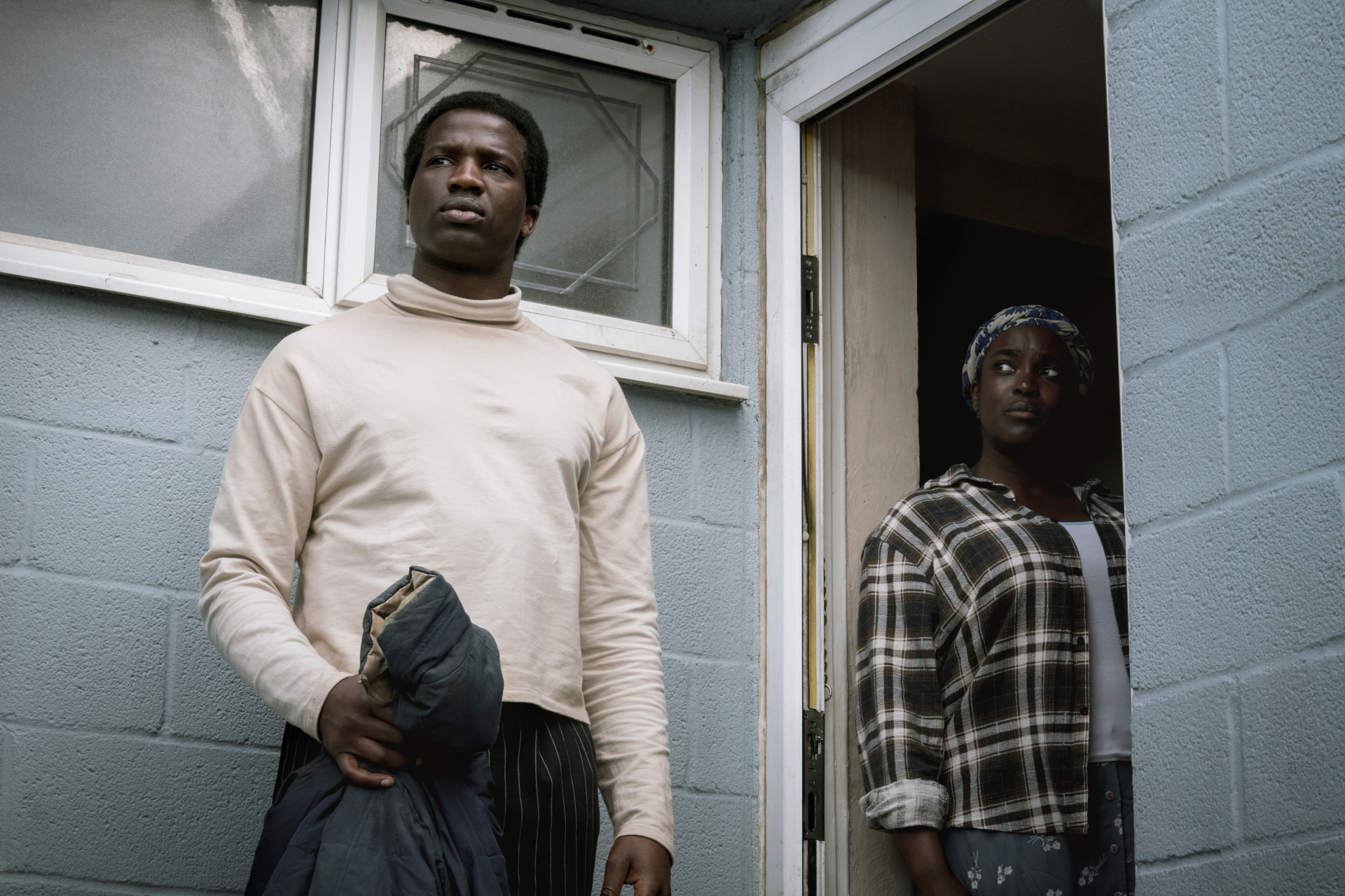 Still from 'His House' showing man and woman at back door of house